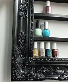 an ornate black framed mirror with nail polish bottles on it's shelf next to a white wall