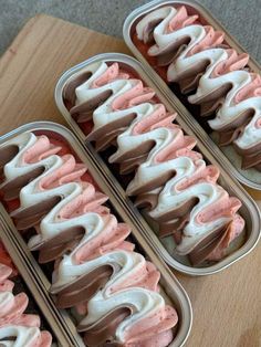 three tins filled with pink and brown ice cream on top of a wooden table