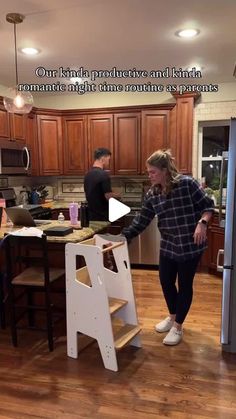 a woman standing next to a step stool in a kitchen with wooden floors and cabinets