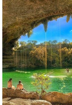 two people sitting on the edge of a cave looking out over a body of water