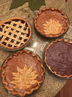 four pies with leaf designs on them sitting on a counter