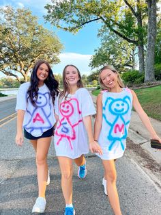 three girls are walking down the street with their hands in each others'pockets and painted letters on them