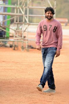 a man walking across a dirt field next to a metal structure