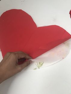 someone is making a heart out of paper on a white surface with a red rose