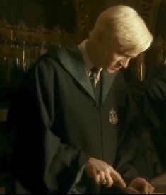 two men in harry potter robes look at something on a table while another man stands behind them