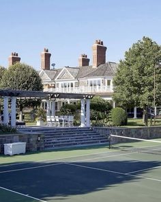 a tennis court in front of a large white house with columns on each side and stairs leading up to the upper level