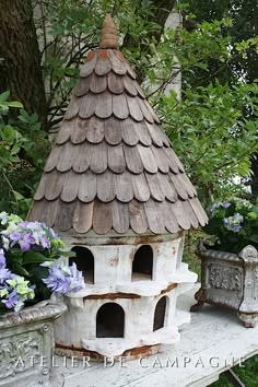 a bird house sitting on top of a white bench next to some flowers and trees