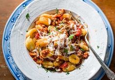 a white plate topped with pasta and meat covered in sauce on top of a wooden table