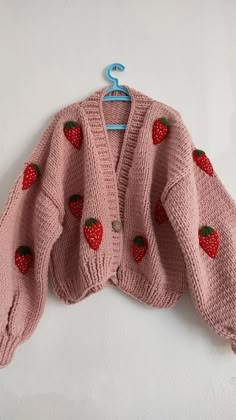 a pink knitted sweater with strawberries on the front and back, hanging from a hook