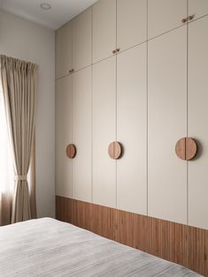 a white bed sitting in a bedroom next to a wall mounted cabinet with three round wooden knobs