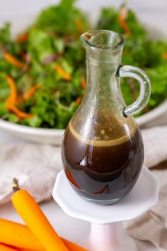 a bowl of salad next to a bottle of liquid and some carrots on a plate