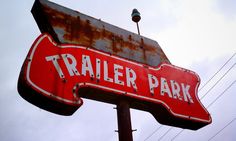 a rusted trailer park sign on top of a wooden pole