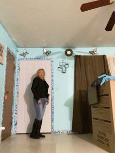 a woman standing in front of a wall with decorations on it and a ceiling fan