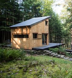 a small wooden cabin in the woods with trees and rocks around it's perimeter