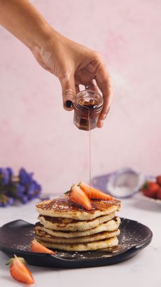 a stack of pancakes with syrup being drizzled over them and topped with sliced strawberries