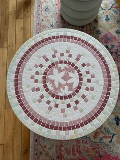 a white and red mosaic tile table on top of a wooden floor next to a potted plant