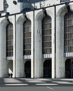 two people are standing in front of an old building with arched windows and large columns