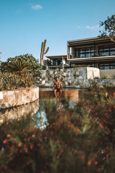 a man sitting on the edge of a pool in front of a building with cactus and cacti