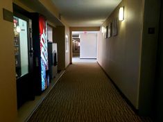 an empty hallway leading to the elevators in a hotel or motel room with posters on the walls