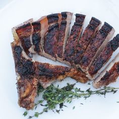 slices of meat sitting on top of a white plate next to some green sprigs