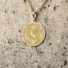 a gold necklace with an image of a bird in the center on a granite surface