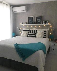 a bed with white sheets and black and white pillows in a room that has lights on the wall above it