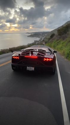 a black sports car driving down the road next to the ocean at sunset or dawn