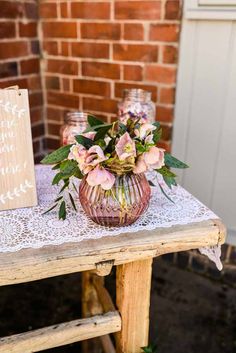 pink flowers in a vase sitting on top of a table next to a wooden sign