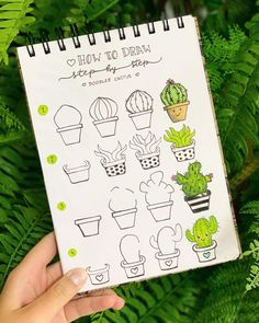 a hand holding up a notebook with drawings on it and green plants in the background