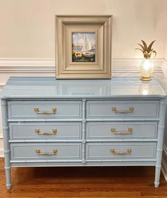 a blue dresser with gold handles and drawers in front of a painting on the wall