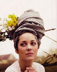 a woman wearing a hat with flowers on it's head and looking at the camera