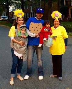 three adults and two children are standing in the street with sesame characters on their heads