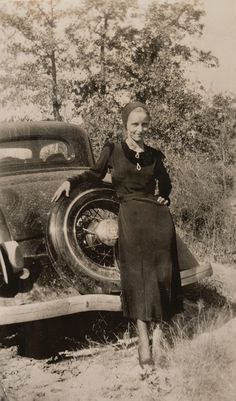 an old black and white photo of a woman standing next to a car