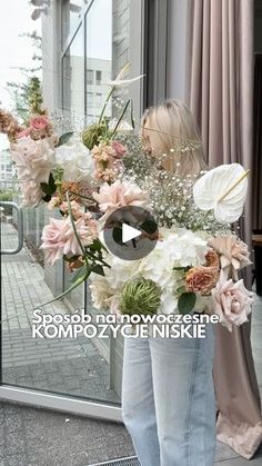 a woman standing in front of a window holding a vase filled with pink and white flowers