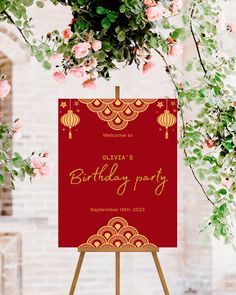 a red and gold birthday party sign sitting on top of a easel next to flowers