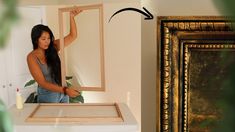 a woman is standing in front of a mirror and painting the frame with her hands