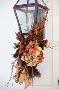 a lantern hanging from the side of a building with flowers and leaves attached to it