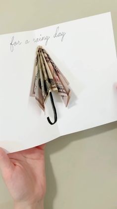 someone holding up a card with an umbrella made out of money and the words for a rainy day written on it