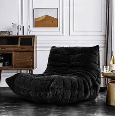 a black bean bag chair sitting in front of a wooden cabinet and side table with wine glasses on it