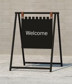 a welcome sign stands in front of a brick wall and concrete sidewalk with the word welcome written on it