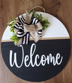 a welcome sign hanging on the side of a wooden door with a bow and greenery