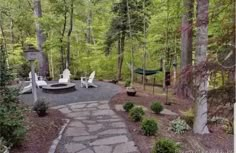 a stone path in the middle of a wooded area with chairs and a hammock