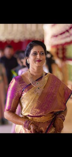 a woman in a purple and gold sari is smiling at the camera with other people behind her