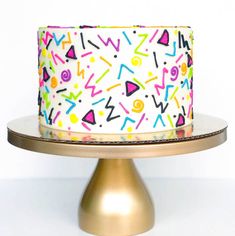 a white cake with multicolored sprinkles is on a gold plate