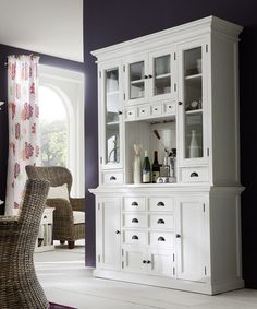 a white china cabinet with glass doors and drawers in a living room area next to a window