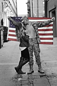 a black and white photo of a man and woman kissing in front of an american flag