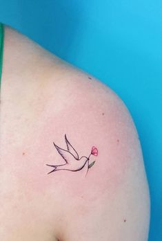 a small tattoo on the back of a woman's left shoulder, with a pink flower in it