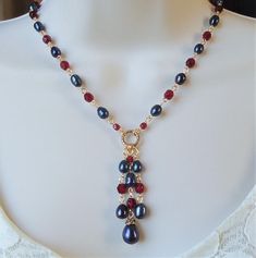 You really can't go wrong with this classic necklace. It is so elegant and versatile, perfect for all seasons. This lariat style necklace combines luminous baroque black pearl with red garnet crystals. It features a decorative infinity circle plated in 24 karat gold. This necklace measures 16" in length, with 2 inches extension.  The pendant-tassel measures 2" in length. This stunning necklace is unique, feminine and eye-catching, Perfect for anyone that wants to make a statement or to wear to a special occasion! Also available in sterling silver plate. Elegant Lariat Jewelry With Dangling Beads, Elegant Single Strand Red Pearl Necklace, Elegant Red Single Strand Pearl Necklace, Elegant Lariat Necklace With Dangling Beads, Elegant Red Necklace With Dangling Beads, Elegant Wire Wrapped Dangle Drop Necklace, Elegant Handmade Lariat Beaded Necklace, Elegant Beaded Lariat Necklace, Elegant Red Drop Necklace