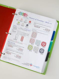 a red and green binder on top of a white table next to a pen