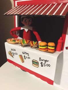 an elf is sitting at a food stand with hamburgers and hot dogs